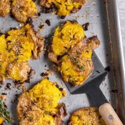 A spatula resting underneath a cirspy smashed potato on a baking sheet.